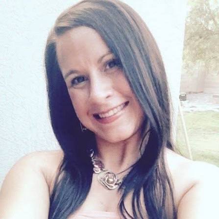 Smiling woman with long dark hair taking a selfie outdoors, wearing a silver necklace.