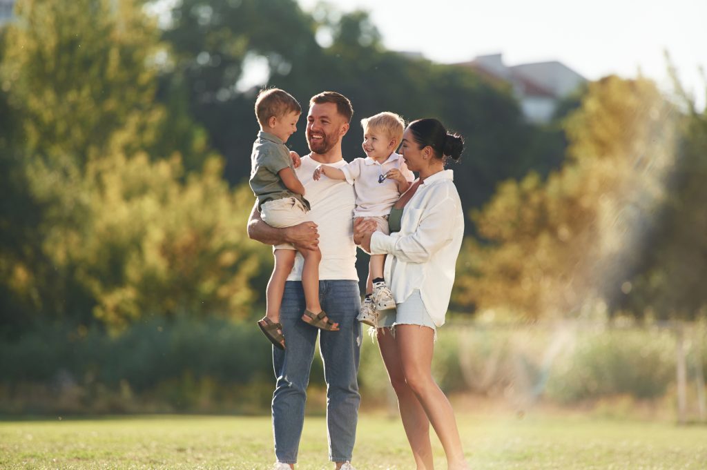 A family of four outdoors in a sunlit park, smiling and enjoying time together.